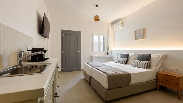 Une chambre moderne avec un grand lit, des tables de chevet, un téléviseur fixé au mur et une fenêtre laissant entrer la lumière naturelle.