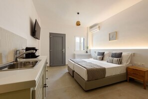 A modern bedroom with a large bed, bedside tables, a TV mounted on the wall, and a window with natural light. - Phaedrus Living: Paros Cycladic Residences 12 (Piso Livadi)