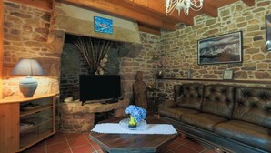 Una sala de estar con paredes de piedra, una chimenea, un televisor, un sofá de cuero y una mesa de centro de madera.
