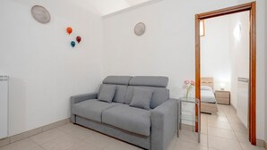 A modern room with a grey sofa, a small table with a vase, and a bed in the background. - GuestHost - Comfortable 53 sqm apartment, perfect for 4 people, located on the ground floor of a building.The property is located in a residential area of ​​Monopoli, a few minutes from the historic center and the main city attractions, in an area fu (Monopoli)