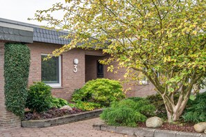 A brick building with a number 3 sign, surrounded by various shrubs and a tree with yellow leaves. - Apartment 'Lortz' with Private Terrace, Shared Garden and Wi-Fi (Cuxhaven)