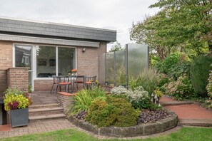 A modern house with a patio, a brick exterior, and a garden with various plants and a small table with chairs. - Apartment 'Lortz' with Private Terrace, Shared Garden and Wi-Fi (Cuxhaven)