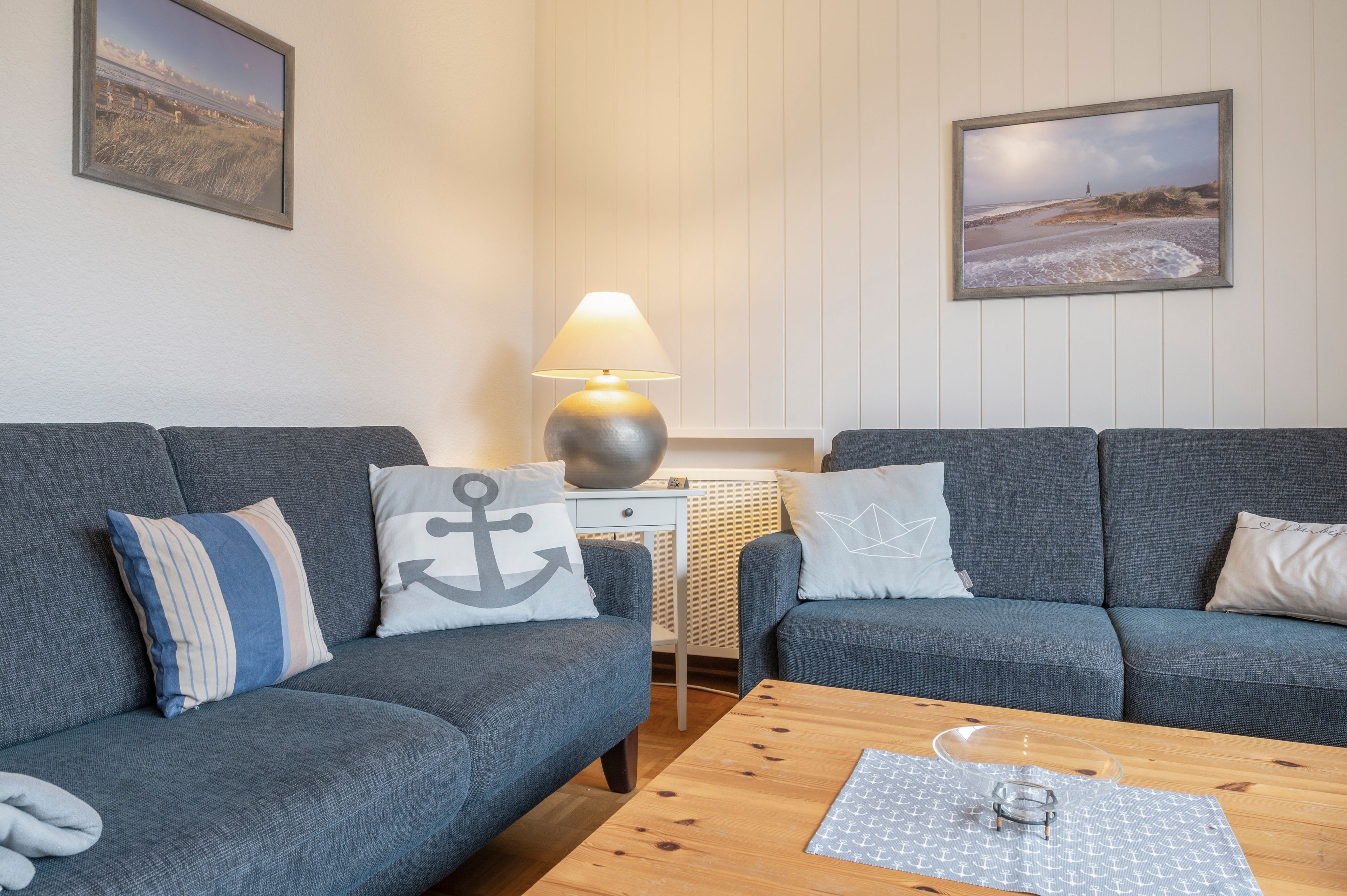A living room with two grey sofas, a wooden coffee table, a lamp, and two wall-mounted pictures.