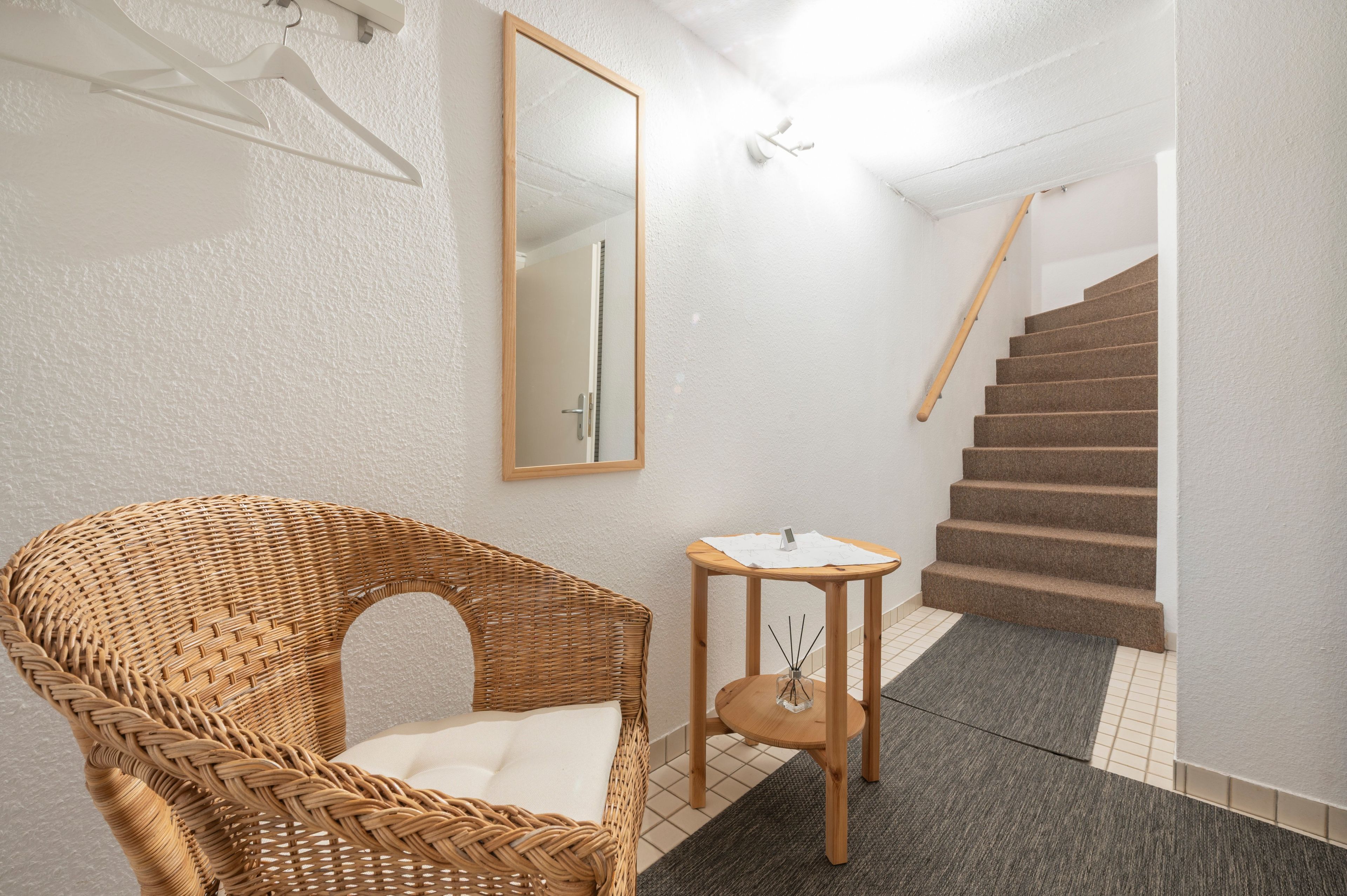 Ein Badezimmer mit einem Korbstuhl, einem kleinen Tisch, einem Spiegel und einer Treppe.