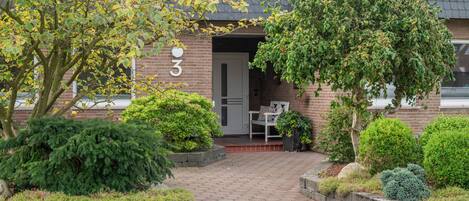 Een bakstenen gebouw met een bord met het nummer 3, een deur en een bankje ervoor.