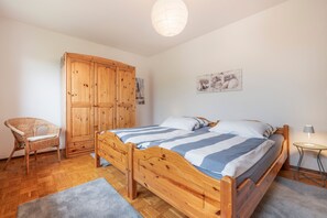 A bedroom with a wooden bed, a wooden wardrobe, a wicker chair, and a painting on the wall. - Apartment 'Lortz' with Private Terrace, Shared Garden and Wi-Fi (Cuxhaven)