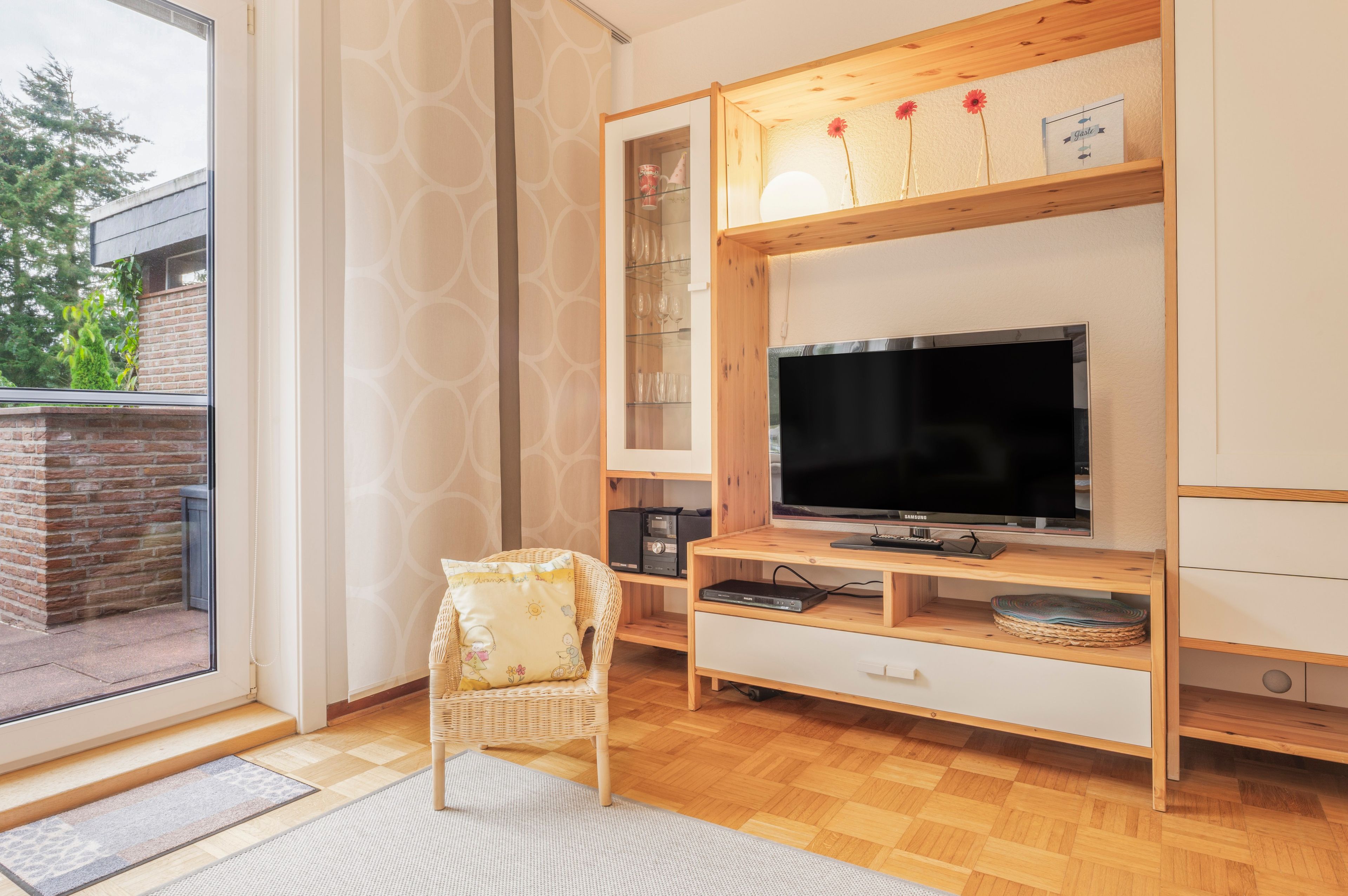 Uma sala de estar moderna com televisão de tela plana, móvel de entretenimento de madeira e uma poltrona de vime.