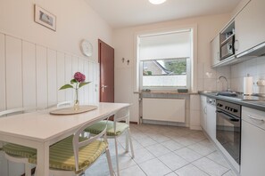A compact kitchen with a dining table, chairs, a window, and a built-in oven. - Apartment 'Lortz' with Private Terrace, Shared Garden and Wi-Fi (Cuxhaven)