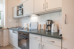 A modern kitchen with white cabinets, a stainless steel range hood, a built-in oven, and a coffee maker. - Apartment 'Lortz' with Private Terrace, Shared Garden and Wi-Fi (Cuxhaven)
