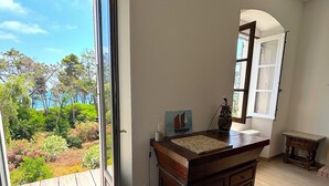Una habitación con un aparador de madera, una mesita pequeña, un cuadro y vistas a un jardín a través de un ventanal amplio.