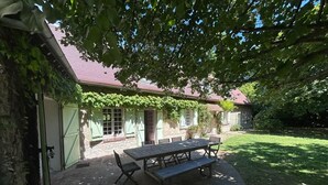 Un bâtiment en pierre avec un toit rouge, un patio couvert avec une table et des chaises, et une porte verte.