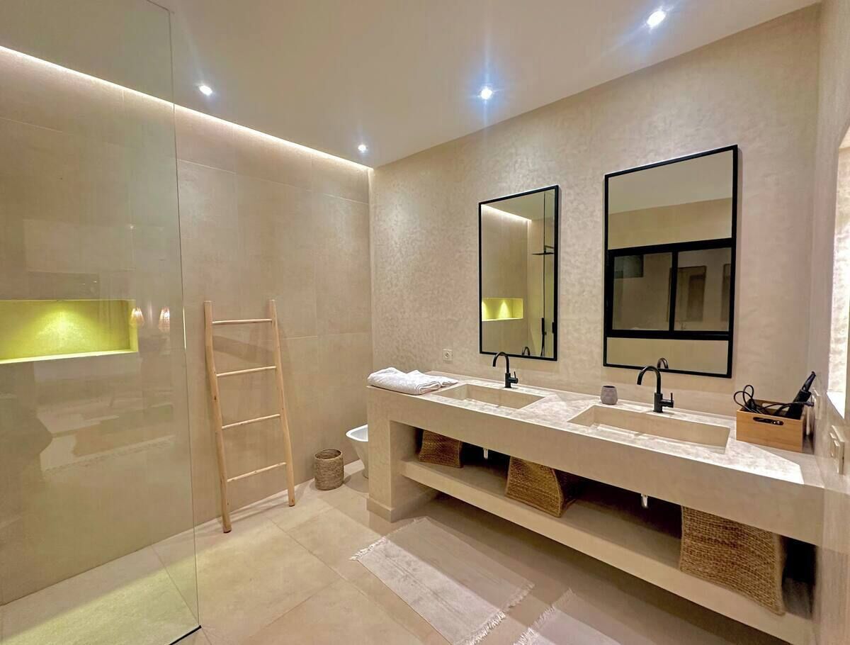 Een moderne badkamer met een douchecabine van glas, een houten trapje, een dubbele wastafel en twee spiegels aan de muur.