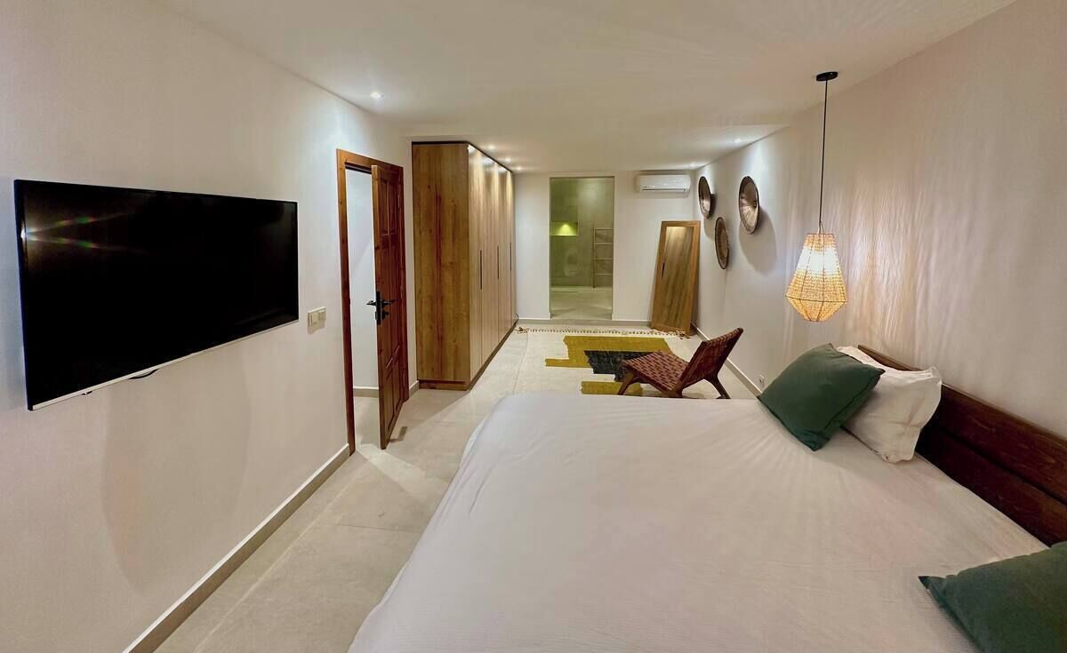Une chambre d’hôtel dotée d’un grand lit, d’un téléviseur à écran plat fixé au mur, d’une armoire en bois, d’une chaise et d’un luminaire suspendu.