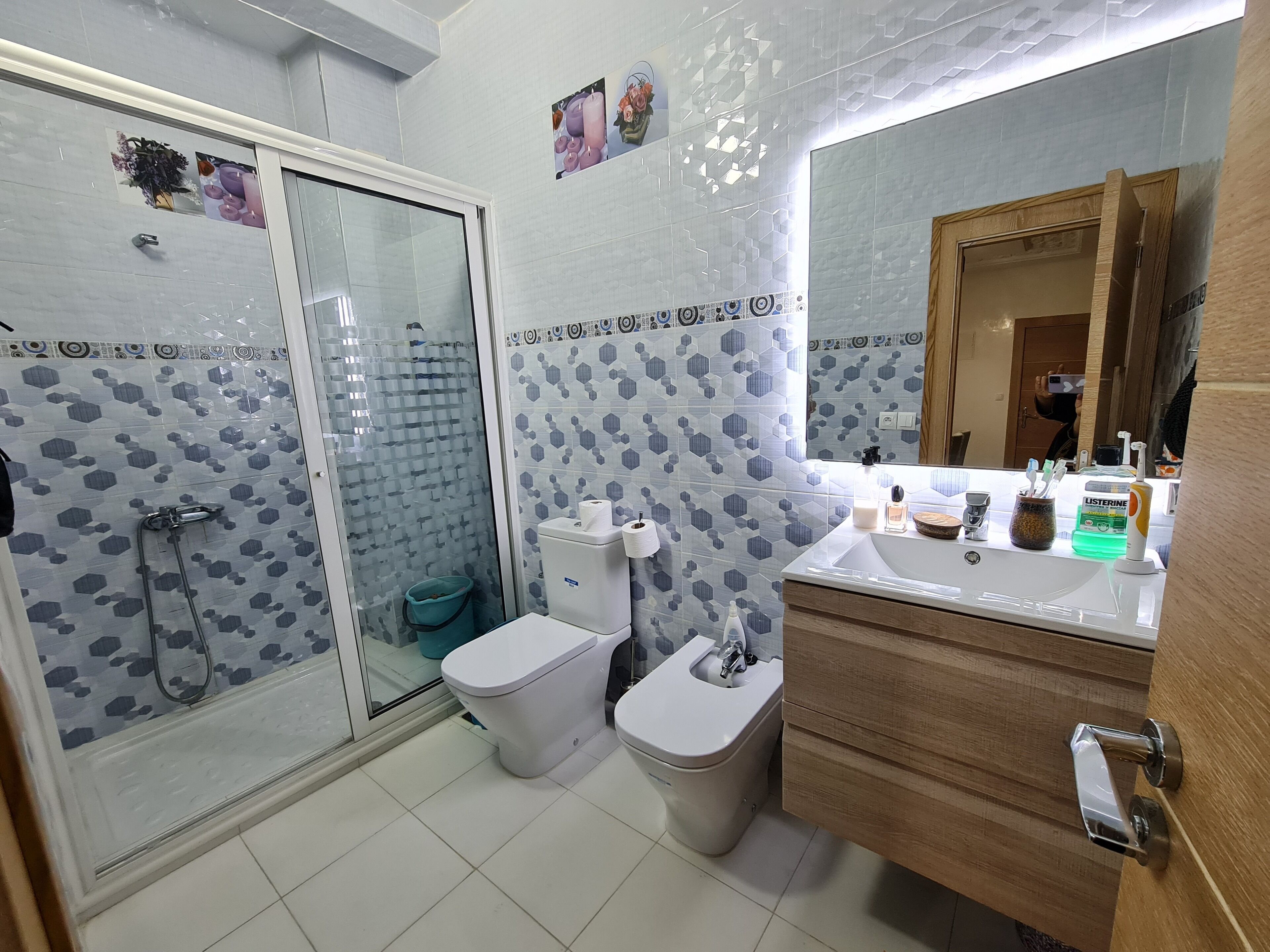 Une salle de bain avec une douche en verre, deux toilettes, un lavabo avec des articles de toilette et un meuble en bois.