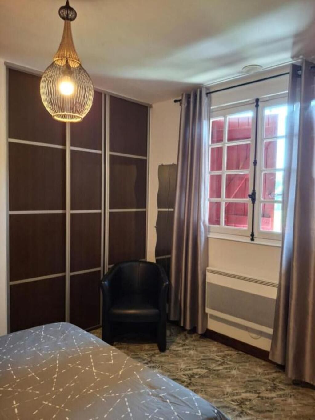 A bedroom with a bed, a chair, a hanging light fixture, and a window with curtains.