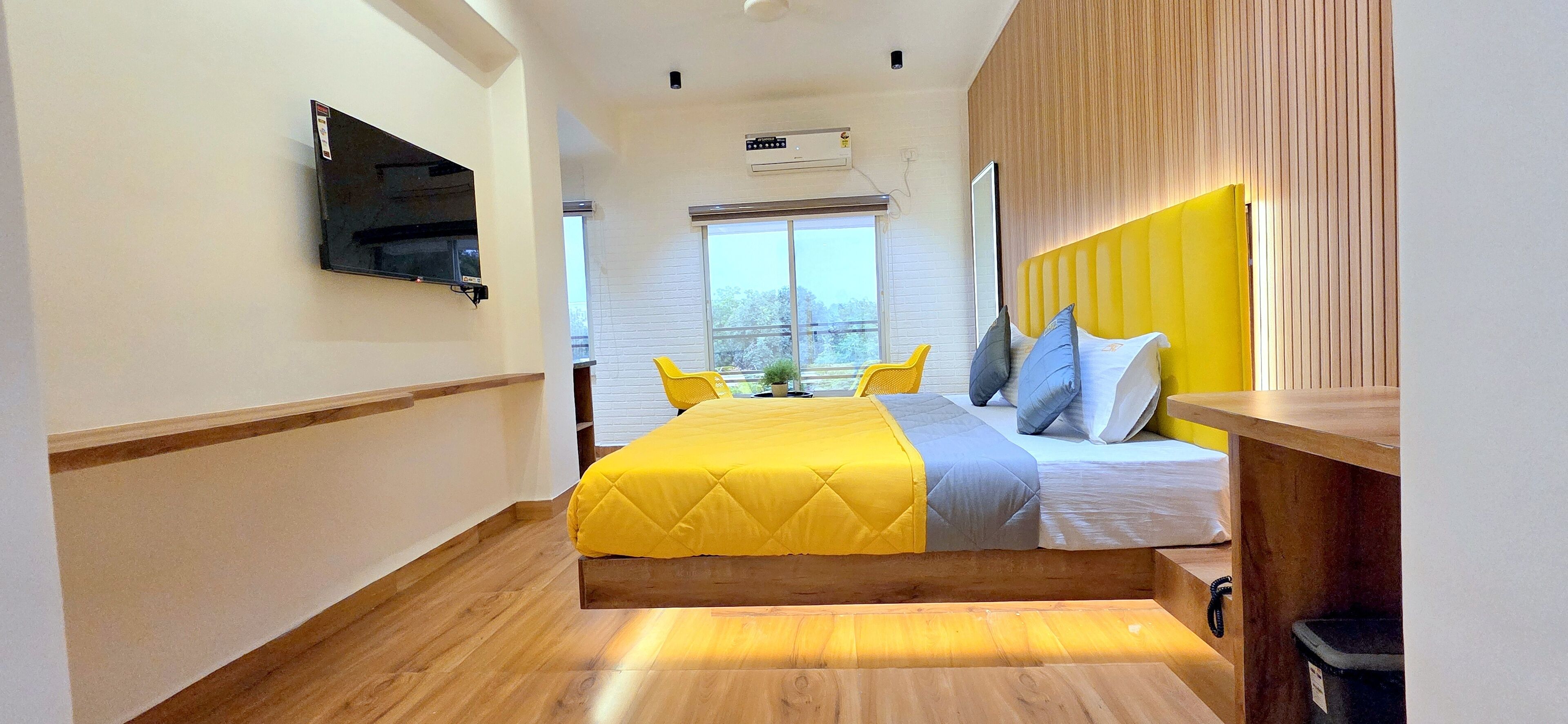 A hotel room with a bed, a TV mounted on the wall, a window, and a balcony.