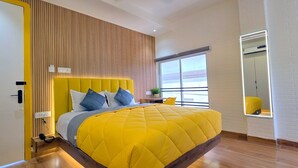 A modern bedroom with a yellow bedspread, a wooden headboard, and a large window offering a view. - Stayinn Suites (Bhopal)