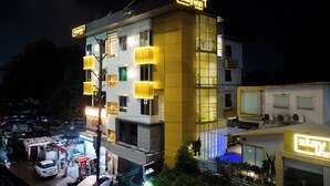 Un hotel a più piani con insegne illuminate, un piano terra visibile con un'auto e un cartello, e una zona con balconi.