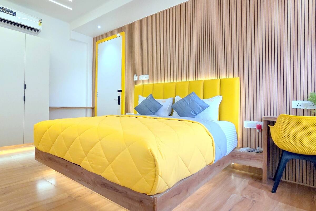 A modern bedroom with a yellow bed, wooden paneling, a built-in microwave, and a small kitchenette.