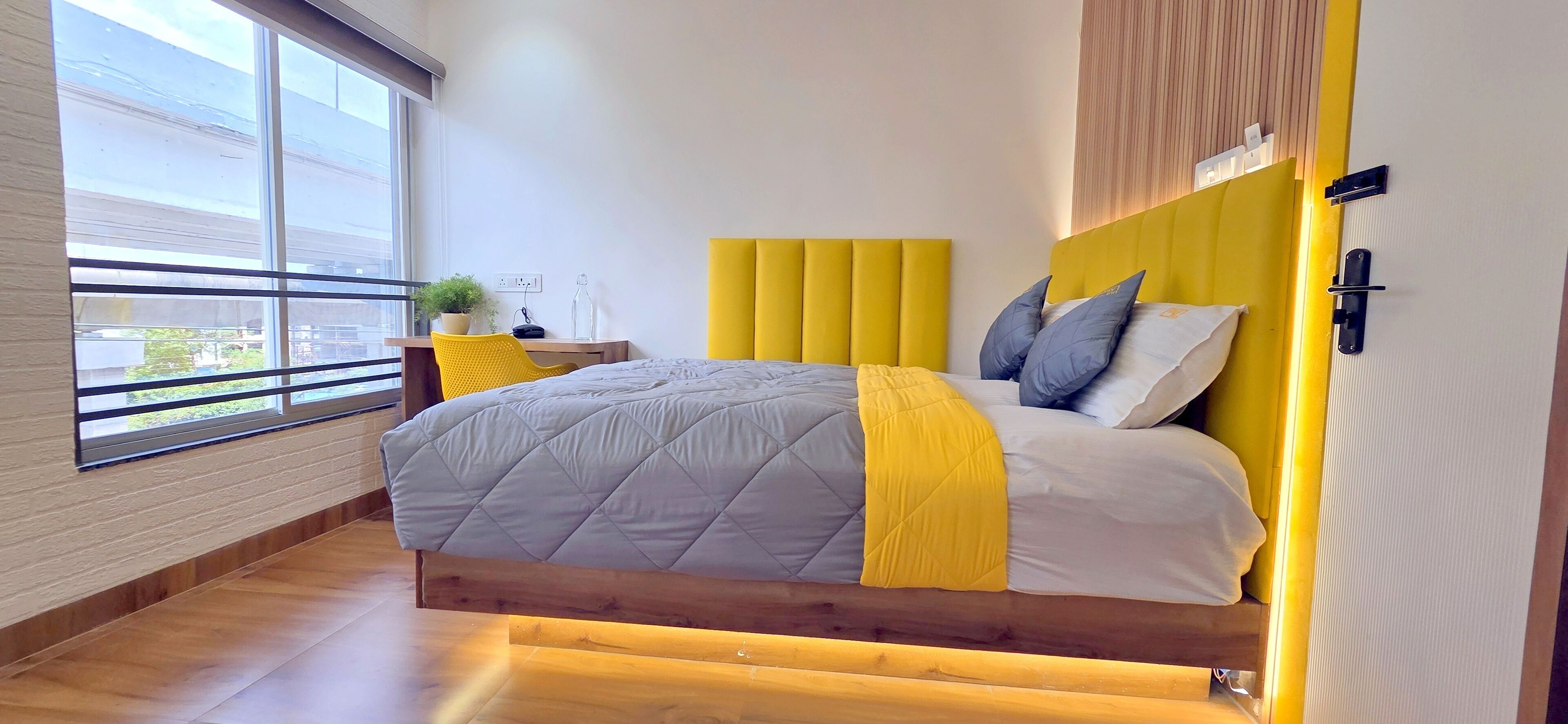 A modern bedroom with a large bed, a yellow headboard, and a view of the outside through a large window.