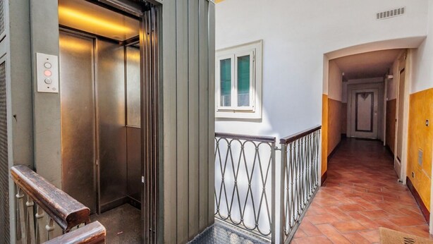 An elevator, a metal railing, a window, and a hallway with a tiled floor.