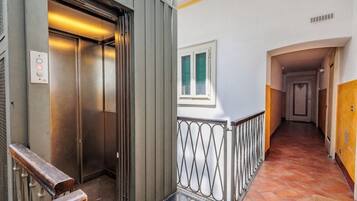 An elevator, a metal railing, a window, and a hallway with a tiled floor.