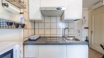 A compact kitchen with white cabinets, a stainless steel sink, a microwave, and a built-in oven.