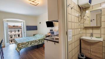 A compact room with a bed, a small kitchenette, a sink, and a mirror.