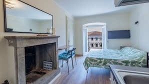 A bedroom with a bed, a fireplace, a mirror, and a view of the outside.