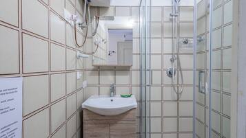 A bathroom with a sink, mirror, shower, and tiled walls.