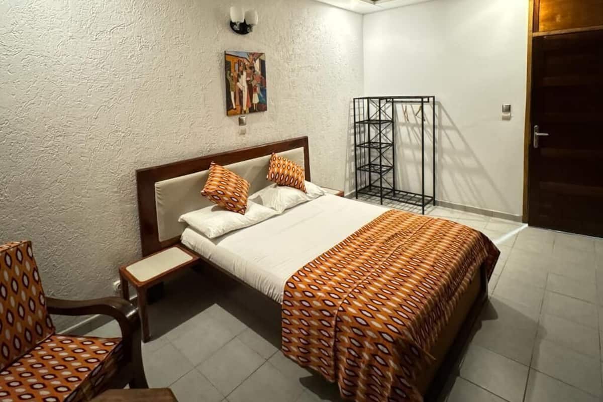 Habitación de hotel con cama, una silla, un cuadro en la pared y una puerta.