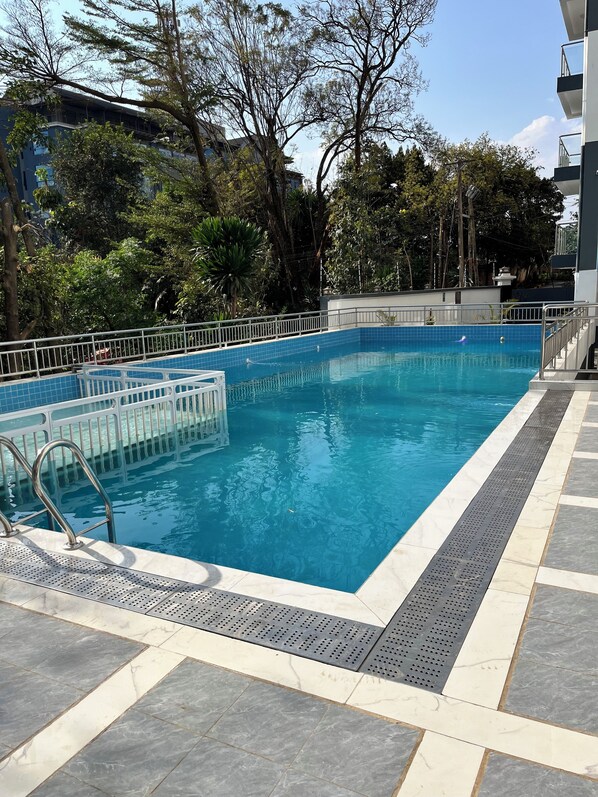 A rectangular swimming pool with a metal safety railing, surrounded by a tiled deck with a tactile path for the visually impaired.