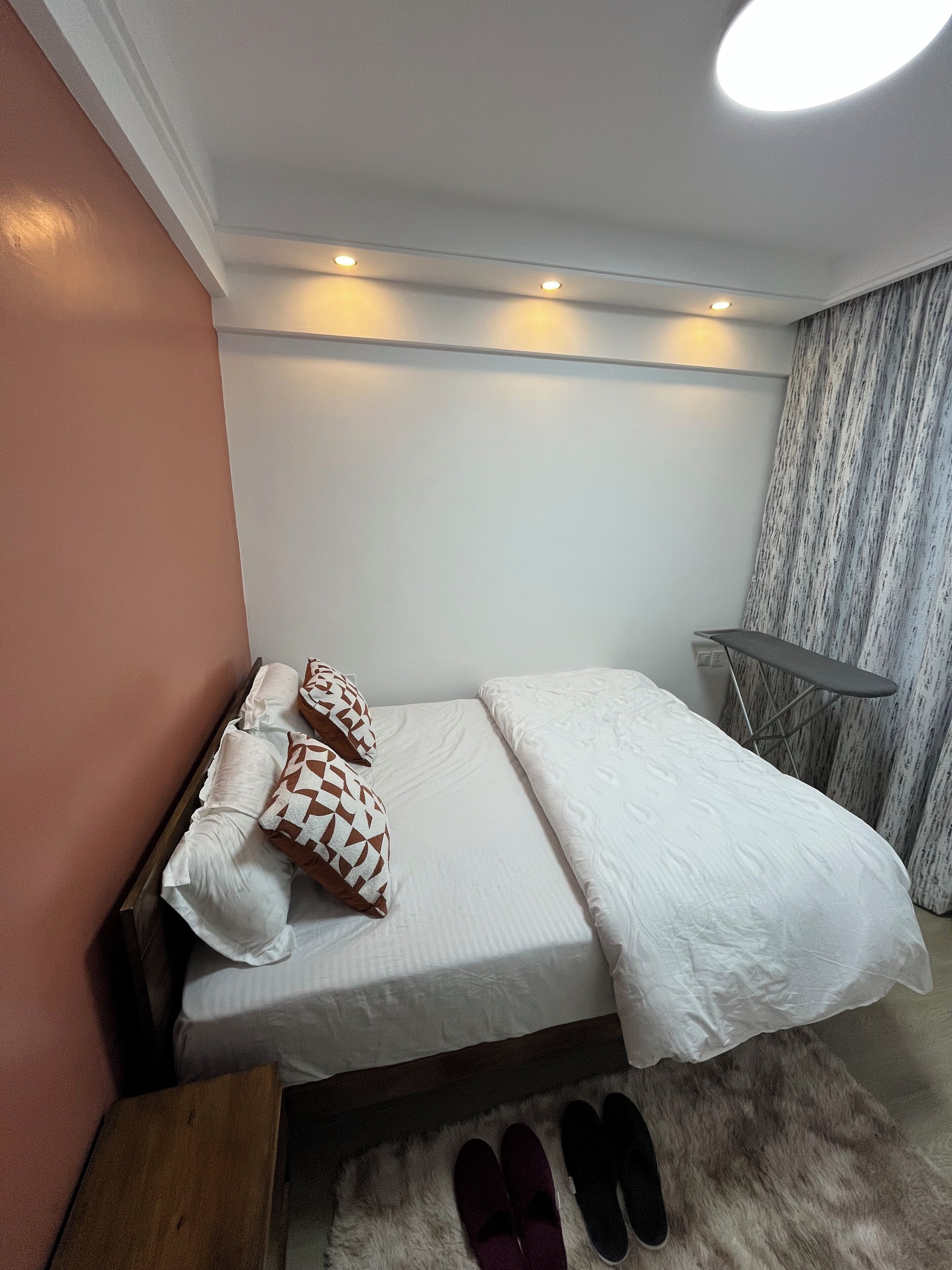 Una cama bien tendida con almohadones estampados, una pequeña mesita de madera y una alfombra de piel en el suelo.