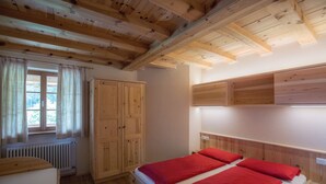 Une pièce avec un plafond en bois, un lit avec une literie rouge, une armoire en bois et une fenêtre avec des rideaux.