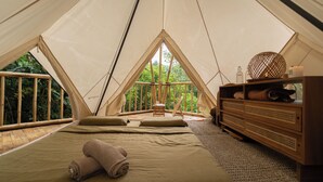 Un hébergement sous tente comprenant un lit, des oreillers, une commode en bois et une petite table.