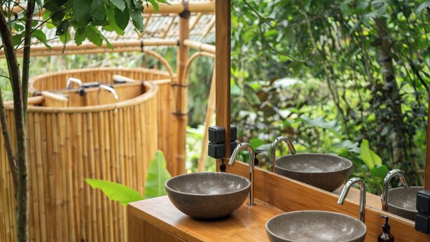 Une salle de bain avec deux vasques sur pied, un miroir et un décor en bambou.