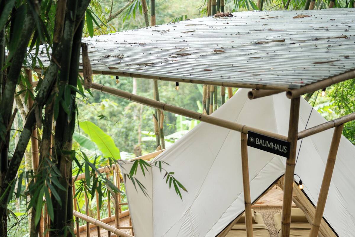 A bamboo structure with a tent labeled "BAUMHAUS" and a wooden staircase leading to it.