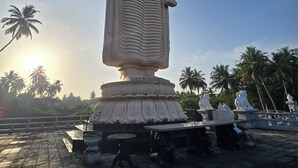 Une grande statue représentant une figure assise, le bras levé, entourée de palmiers et se dressant sous un ciel dégagé.