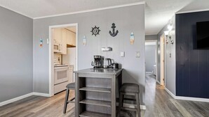 Cocina compacta con microondas, cafetera y una pequeña isla con taburetes.