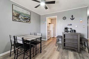 A dining area with a table and chairs, a ceiling fan, a kitchen in the background, and nautical-themed wall decor.