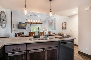 A modern kitchen with a central island, pendant lights, a fireplace, and a dining area.
