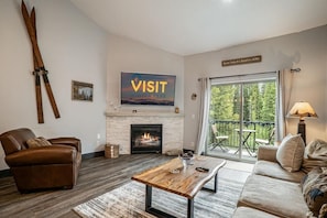 A living room with a fireplace, a large window with a view, a sign reading 'VISIT WINTER PARK,' and a sign indicating the property's elevation.