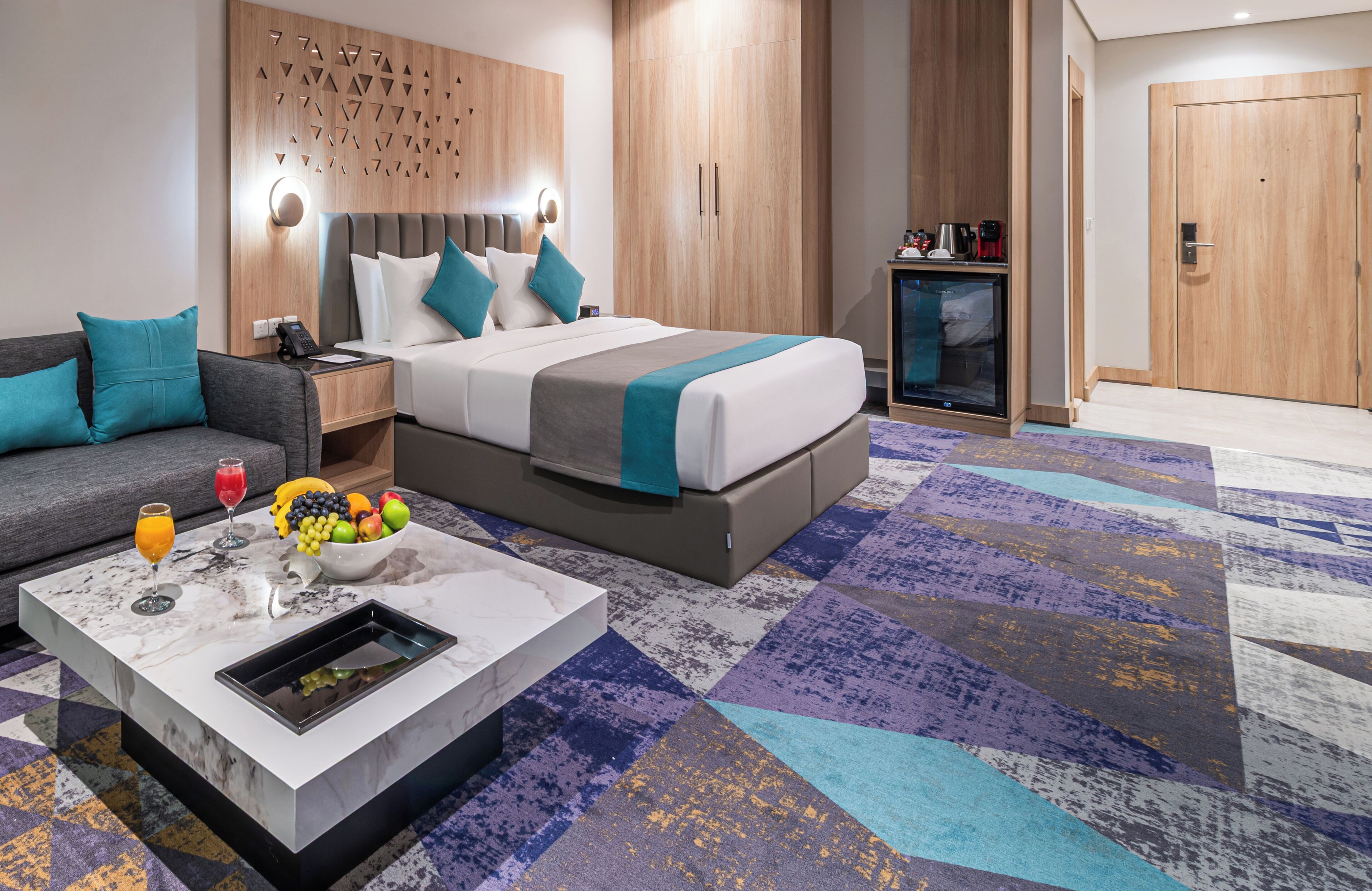 Une chambre d’hôtel moderne équipée d’un lit, d’un canapé, d’une machine à café et d’un panier de fruits.