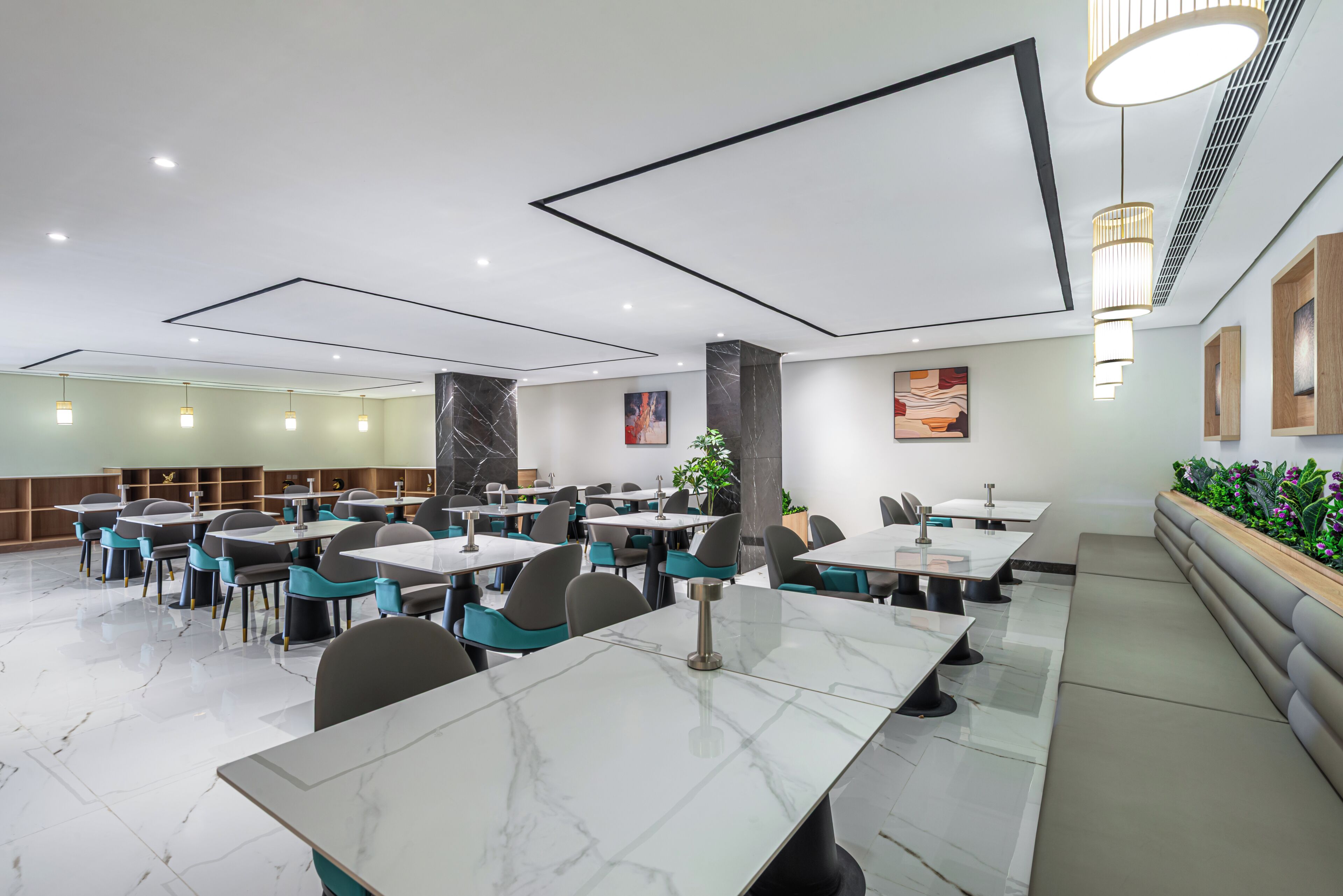 A modern dining area with marble tables, teal chairs, and pendant lighting.