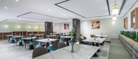 A modern dining area with marble tables, teal chairs, and pendant lighting.