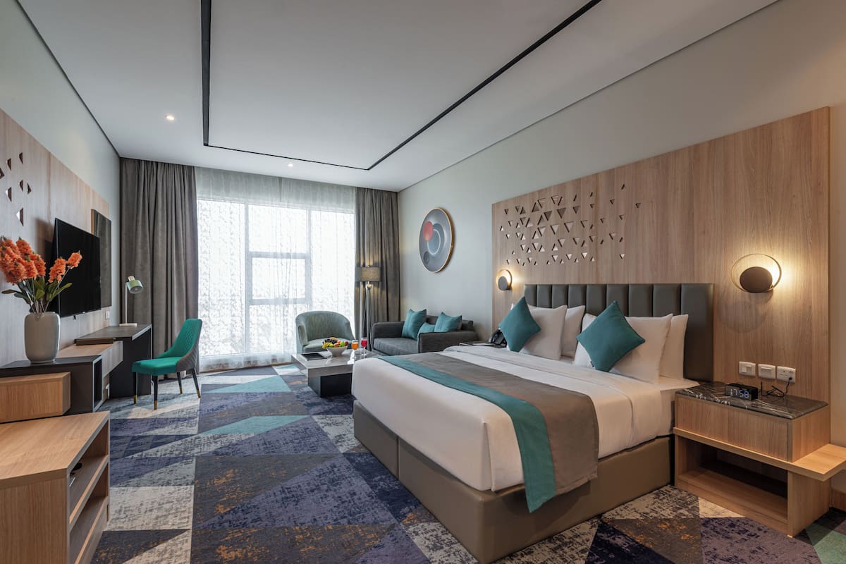 Una habitación de hotel moderna con una cama grande, un escritorio, una silla, un sofá y un televisor.