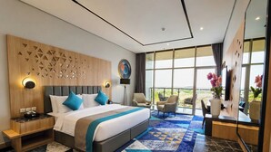 A modern hotel room with a large bed, a wooden headboard, a patterned carpet, and a view of the outdoors. - Rhenium Hotel - Abha (Abha)