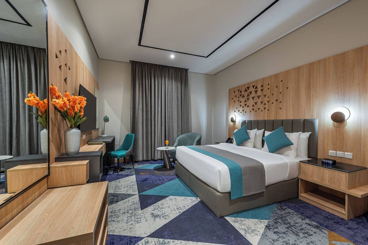 Una habitación de hotel con cama, escritorio, silla, mesita y espejo.