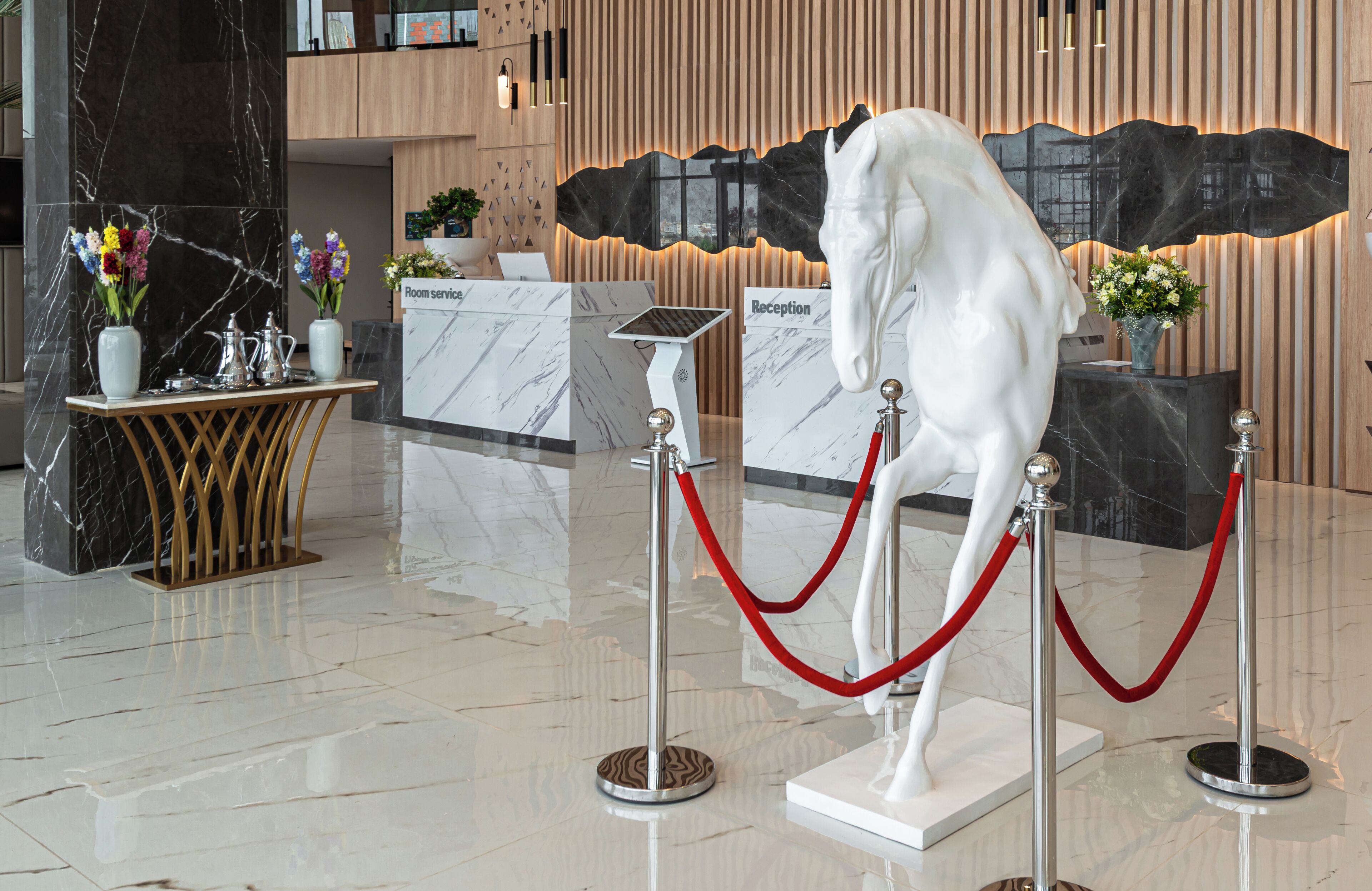 A reception desk with a 'Reception' sign, a white horse statue, and a red rope barrier.