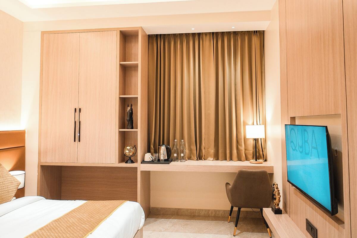 A hotel room with a bed, a desk with a computer, a TV, and a wardrobe.